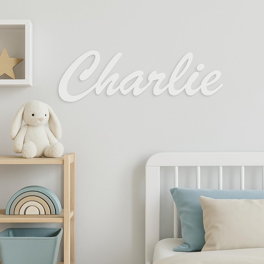 Sticker prénom blanc « Charlie » collé au mur d'une chambre d'enfant, au-dessus d'un lit et d'une étagère