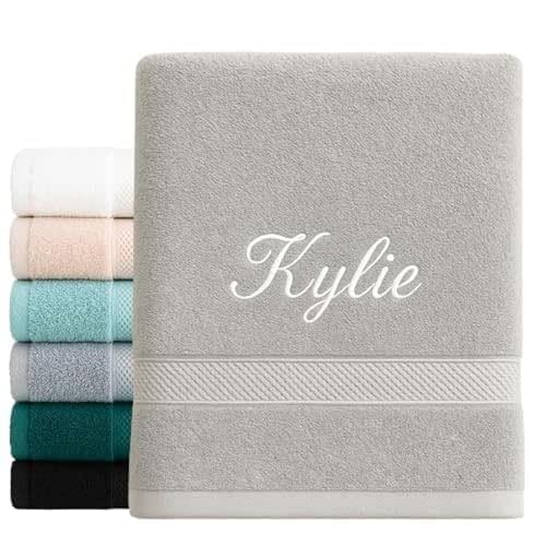 Serviette grise brodée du prénom « Kylie » en fil blanc, devant une pile de serviettes de couleurs