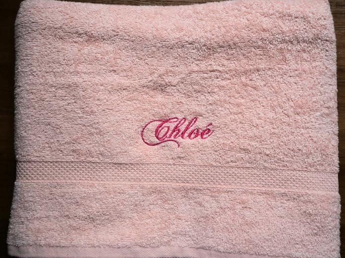 Serviette éponge rose à plat, prénom « Chloé » brodé en fil fuchsia au-dessus de la bordure