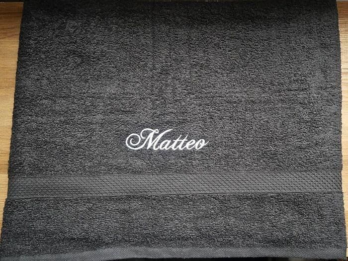 Serviette éponge noire à plat, prénom « Matteo » brodé en fil blanc au-dessus de la bordure