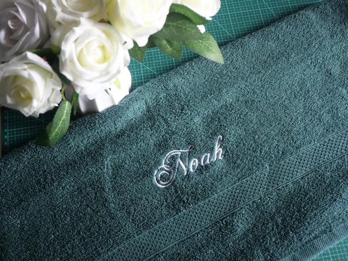 Gros plan du prénom « Noah » brodé en fil blanc sur une serviette éponge verte, roses blanches à côté