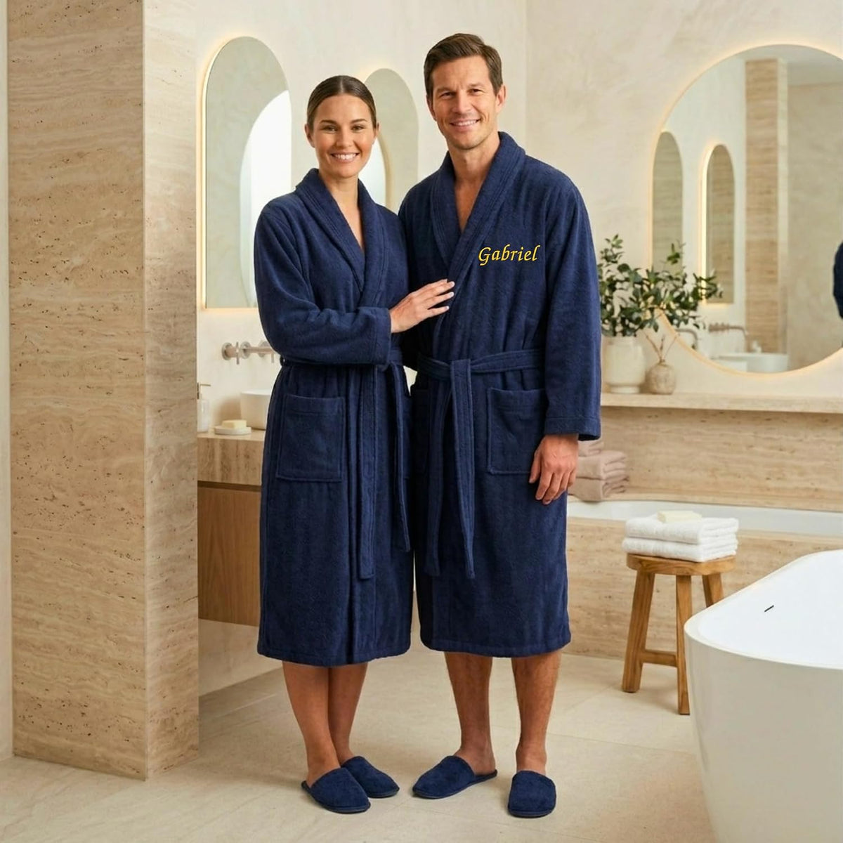 Couple en peignoirs bleu marine dans une salle de bain, celui de l'homme brodé « Gabriel » en fil doré