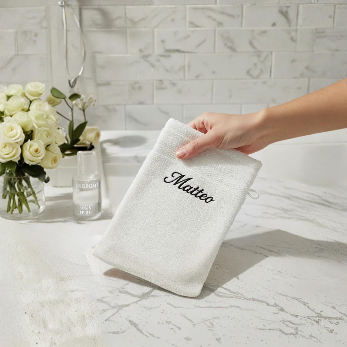 Gant de toilette blanc brodé « Matteo » posé sur un plan de salle de bain en marbre, roses blanches