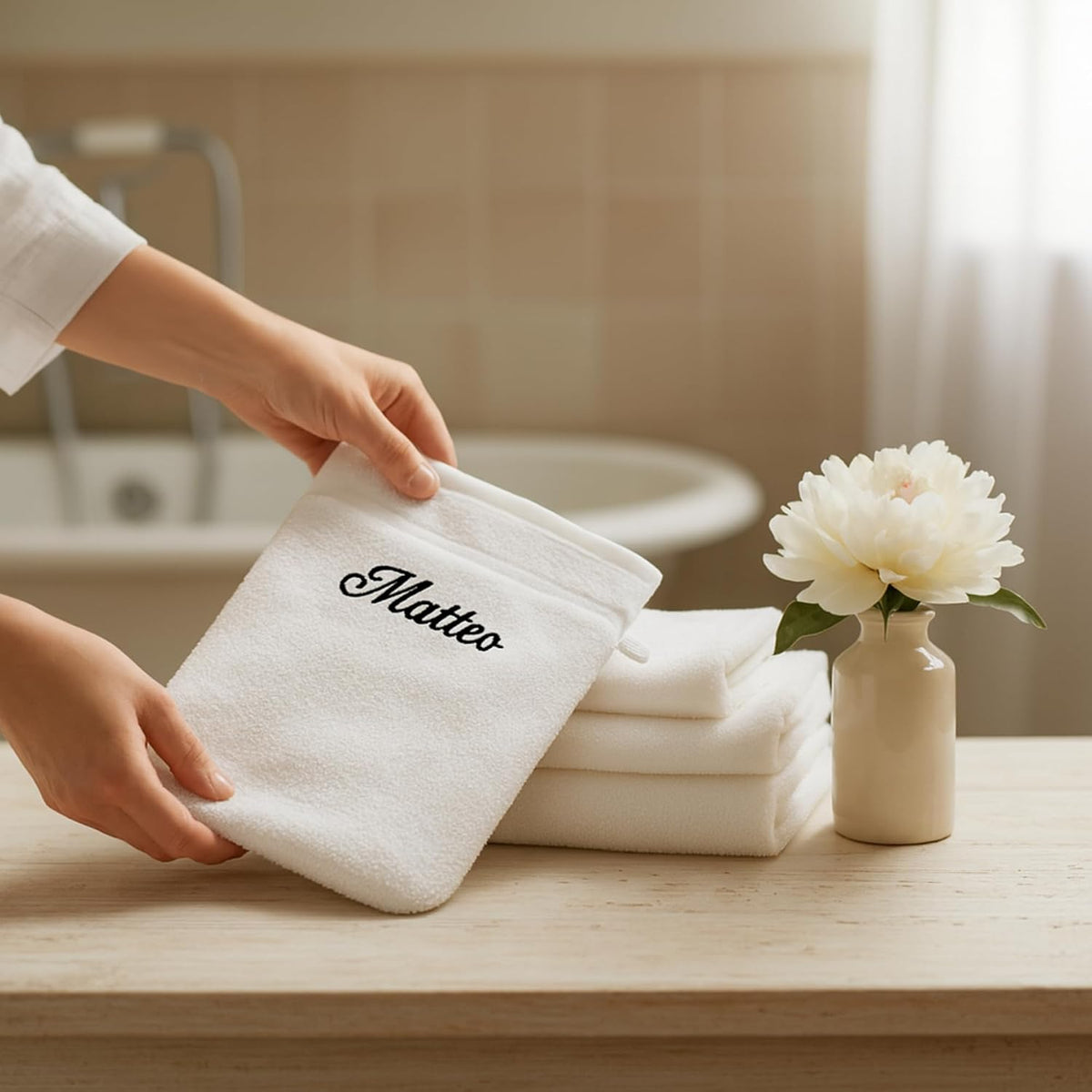 Gant de toilette blanc brodé « Matteo » en noir, présenté dans une salle de bain avec serviettes blanches