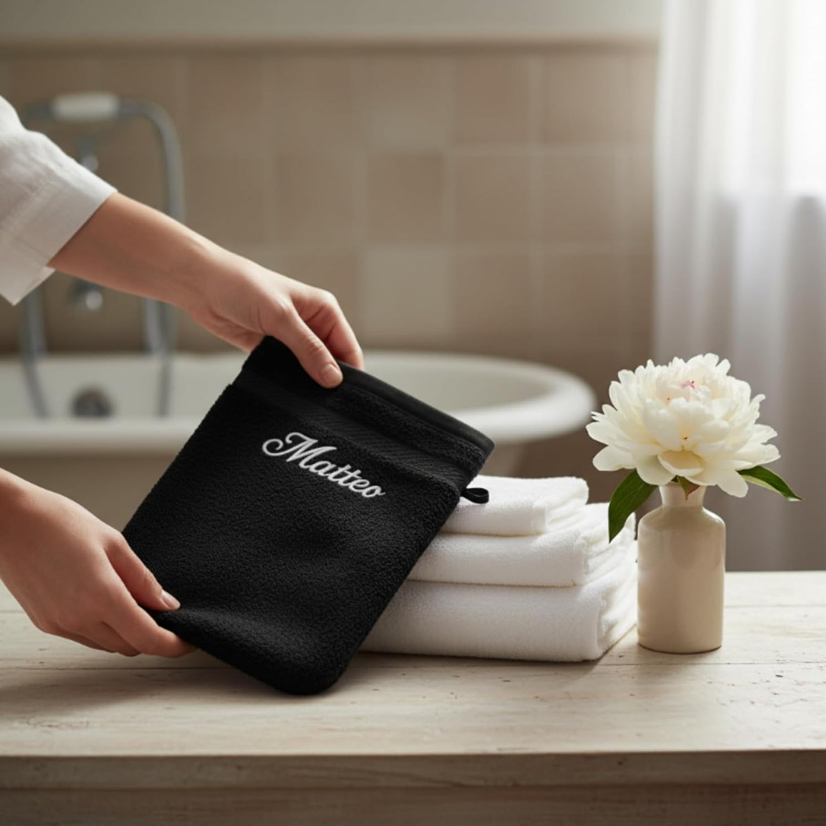 Gant de toilette noir brodé « Matteo » présenté dans une salle de bain, serviettes blanches à côté