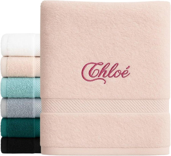 Serviette rose poudré brodée du prénom « Chloé » en fil framboise, devant une pile de serviettes